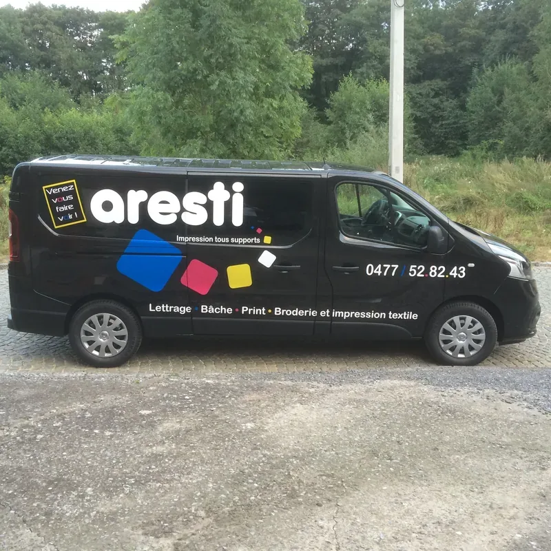 Logo coloré et accroche publicitaire sur la carrosserie noire d'un fourgon Renault.