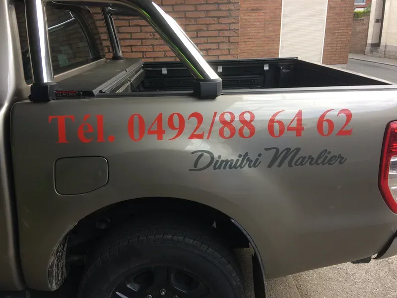 Numéro de téléphone et nom floqués en rouge sur le hayon d'une camionnette.