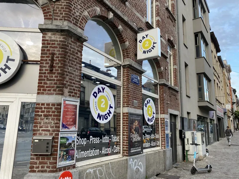 Devanture d'angle en briques avec logos ronds et lettrage sur vitrine, magasin de presse.
