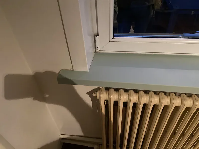 Détail de la finition d'angle d'une tablette de fenêtre habillée en bleu-gris mat.