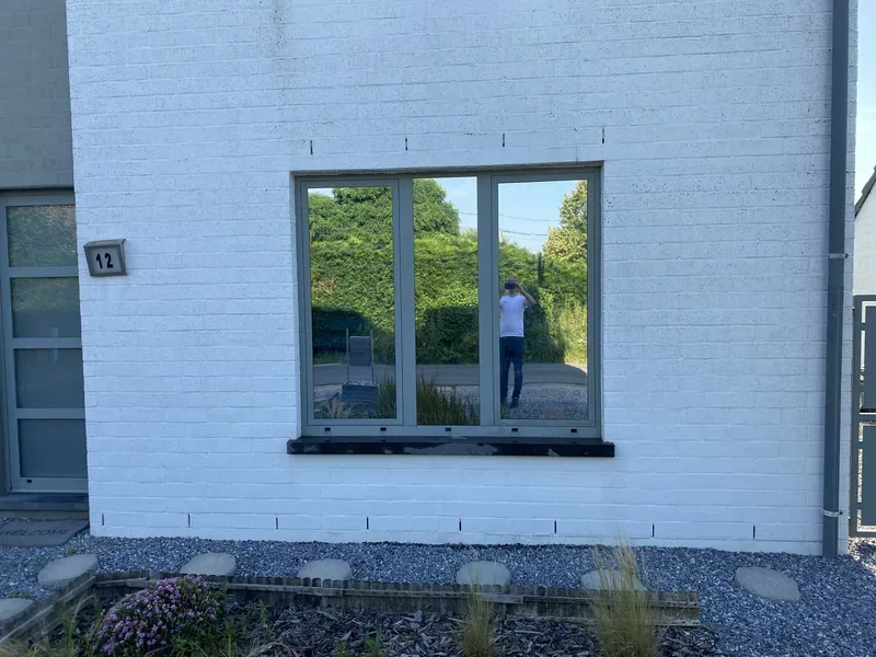 Trois fenêtres traitées anti-chaleur reflétant le jardin sur une façade blanche.
