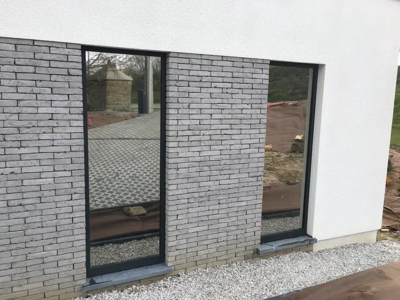 Fenêtres à l'effet miroir marqué sur une façade en briques grises.
