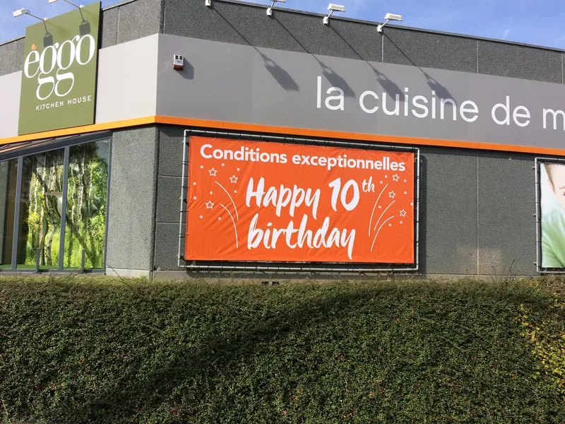 Grande bâche orange annonçant un anniversaire, tendue sur la façade d'un magasin de cuisines.