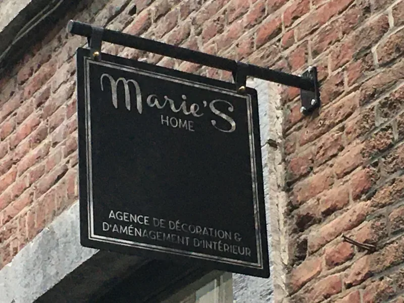 Enseigne noire et argentée suspendue en façade, lettrage soigné pour une agence de décoration.