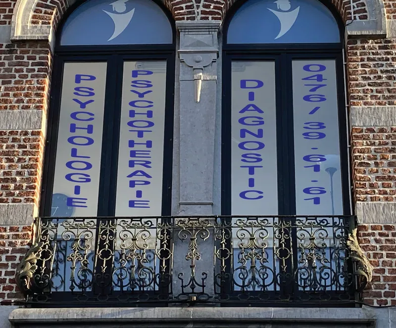 Lettrage bleu sur les fenêtres en arc d'un cabinet de psychologie, façade en briques.