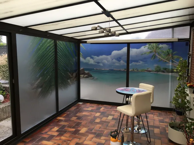 Baies vitrées de véranda recouvertes d'un film décoratif façon plage tropicale.